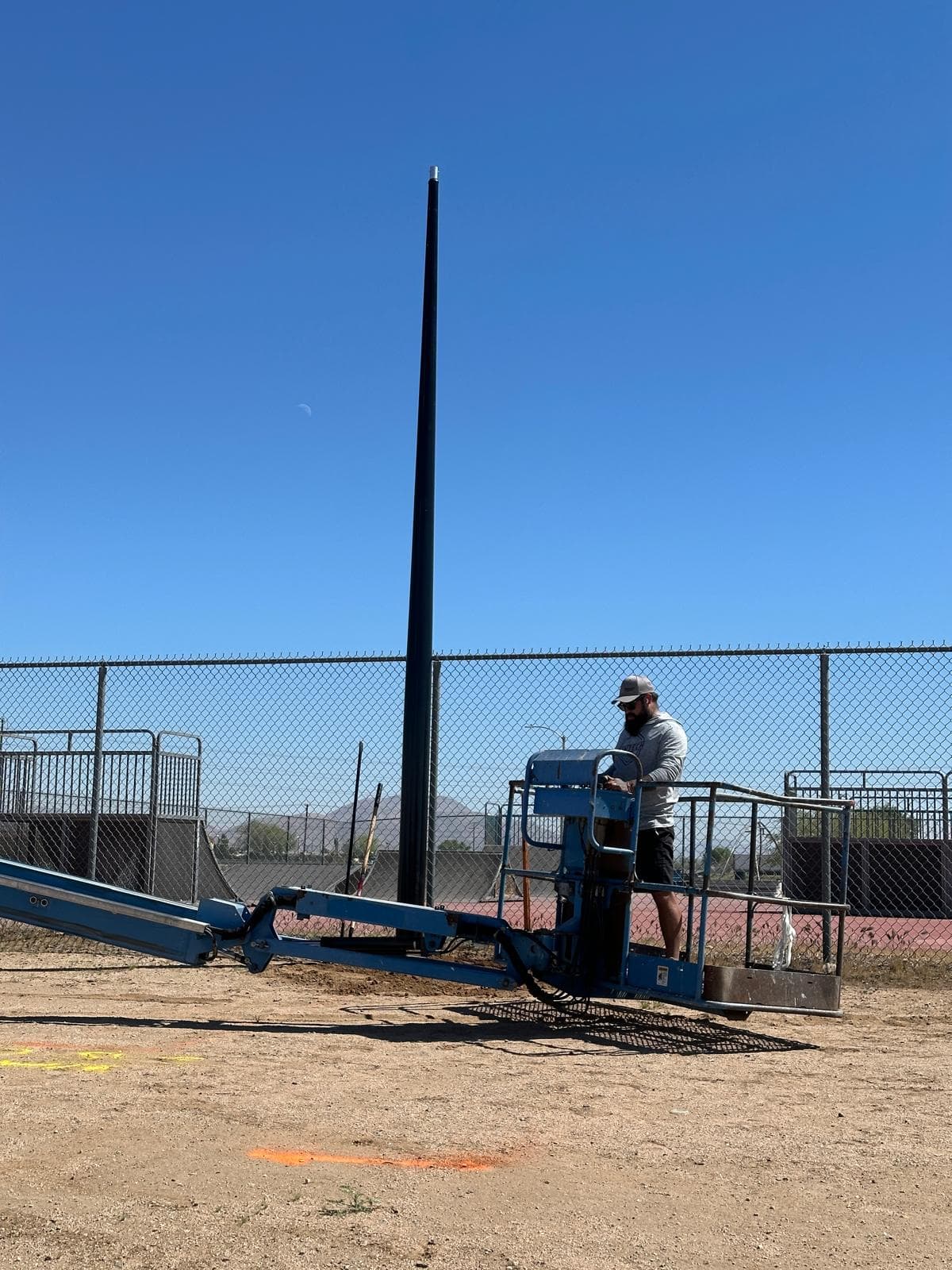 All Seasons pole being raised on site at the Adelanto sports complex, articulated lift in foreground with a worker on the platform