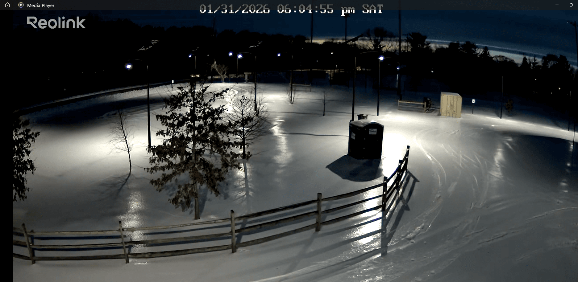 Reolink security camera screenshot of Riverview Park at night during winter, snow on the ground, All Seasons poles lit
